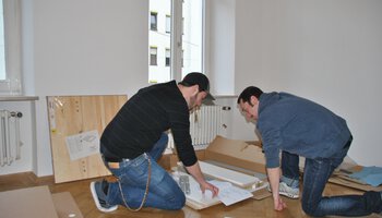 Zwei Männer bauen ein Möbelstück zusammen | © Caritasverband München
